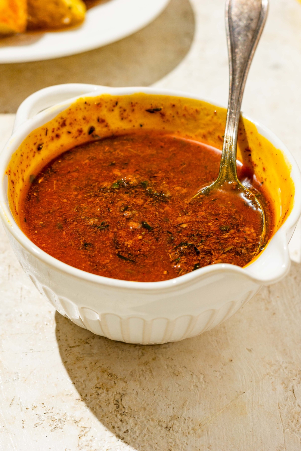 A bowl of cajun garlic butter sauce with a spoon in the bowl. The bowl is on a tan counter.