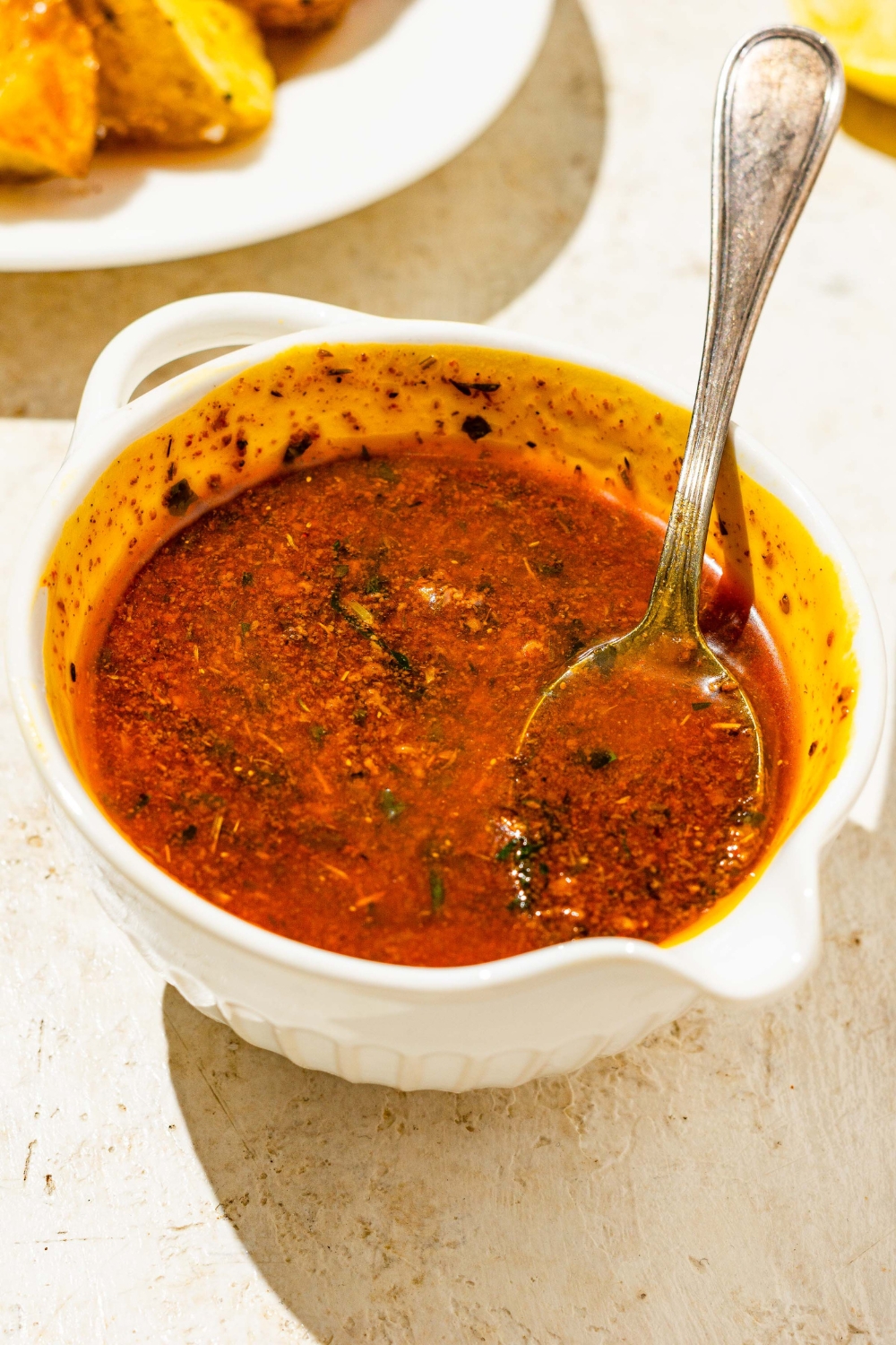 A bowl of cajun garlic butter sauce with a spoon in the bowl. The bowl is on a tan counter.