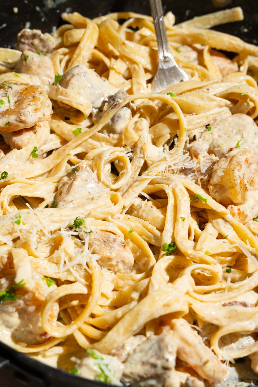 A skillet with a fork tossing chicken and shrimp alfredo garnished with fresh parsley.