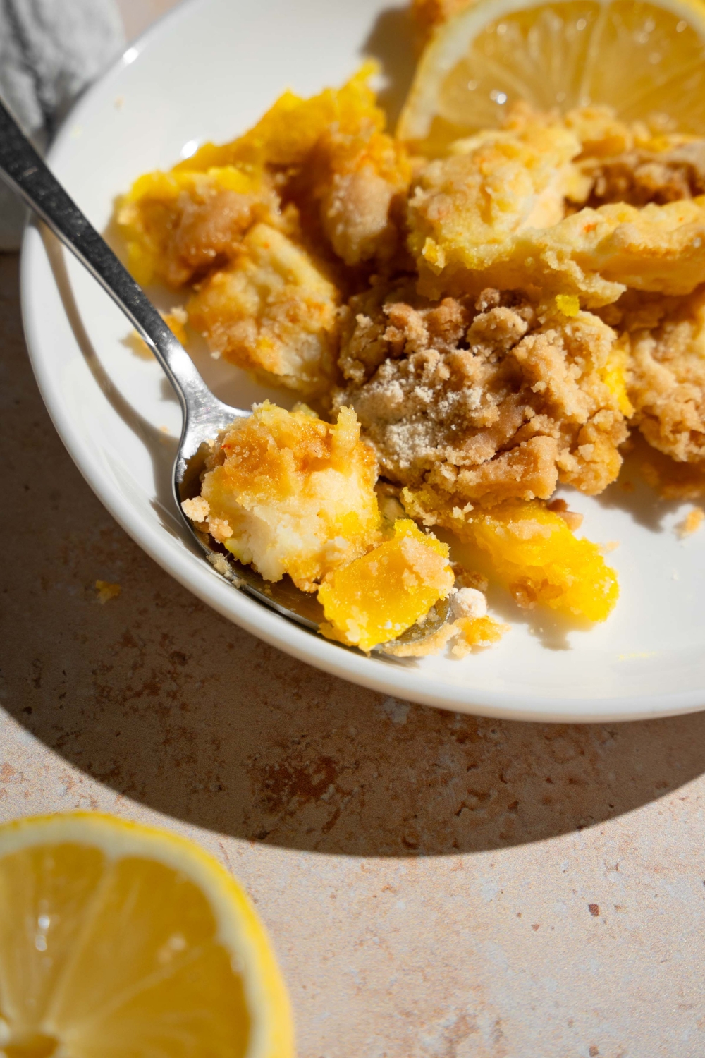 A white plate with a slice of lemon cream cheese dump cake served with sliced lemon and a fork.