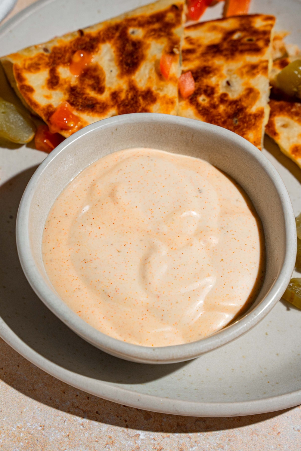 A small bowl of Taco Bell quesadilla sauce on a white plate with sliced quesadilla garnished with pickled jalapenos.