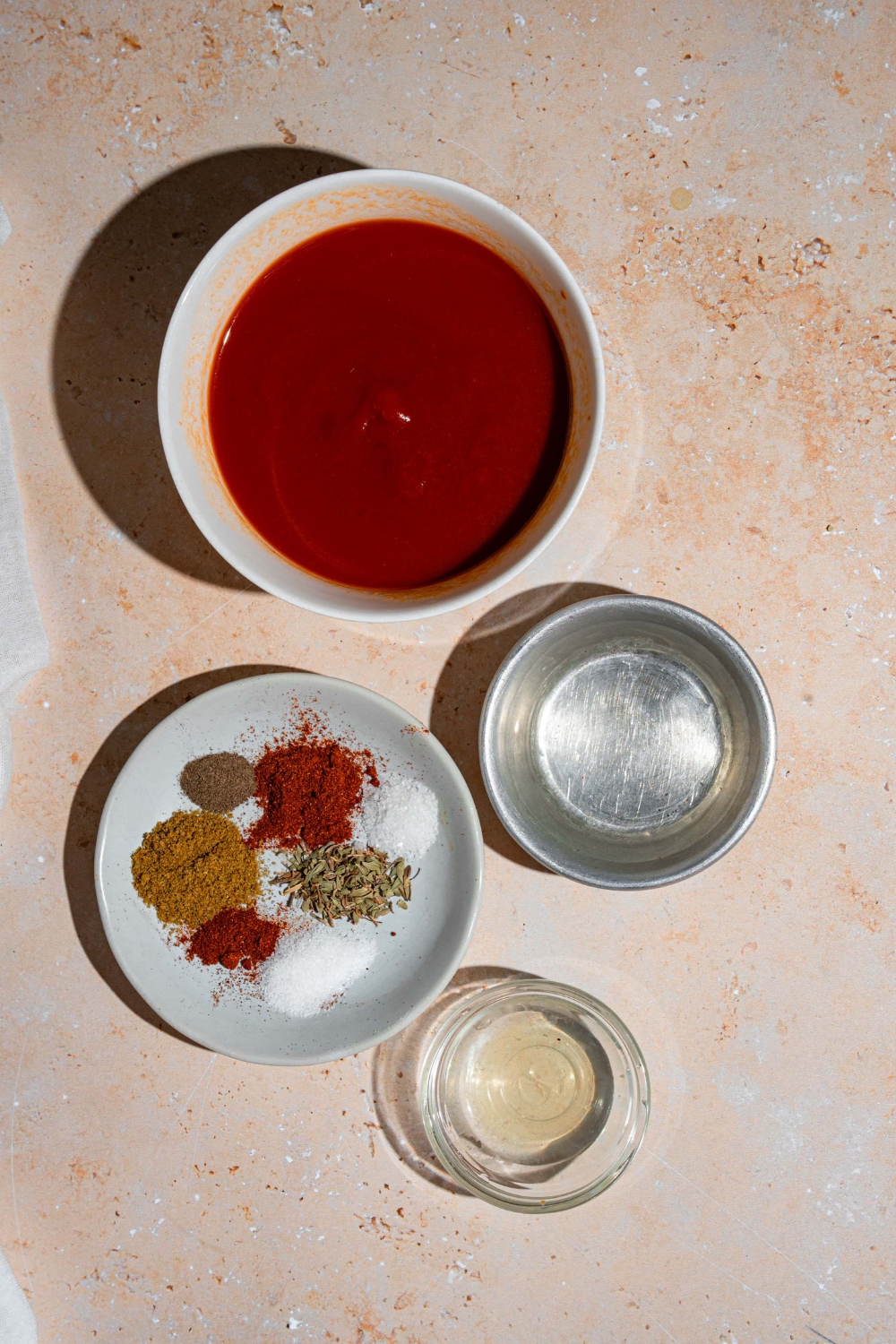 An overhead shot of several bowls in various sizes containing ingredients to make taco sauce including tomato sauce, water, lime juice, and spices.