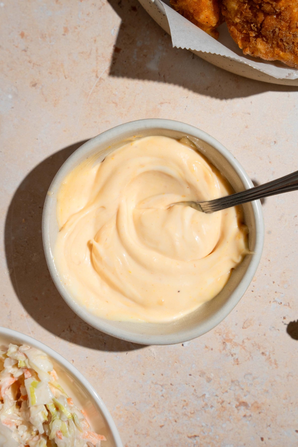 A small bowl with a spoon mixing homemade Chick Fil A sauce. The bowl is on a tan counter with a plate of nuggets.