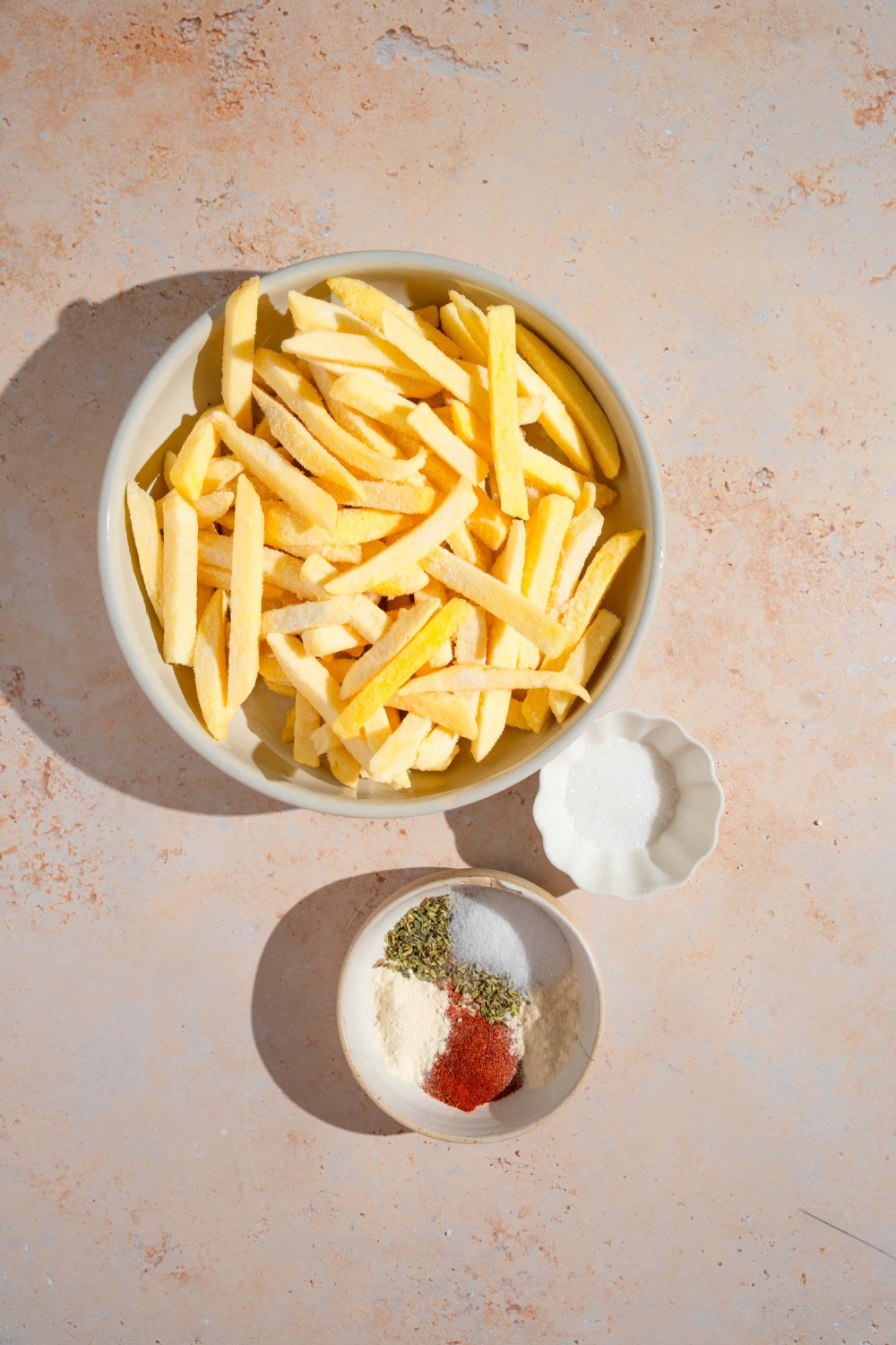 An overhead shot of bowls in various sizes containing ingredients to make Wingstop fries including frozen french fries, sugar, and seasonings.