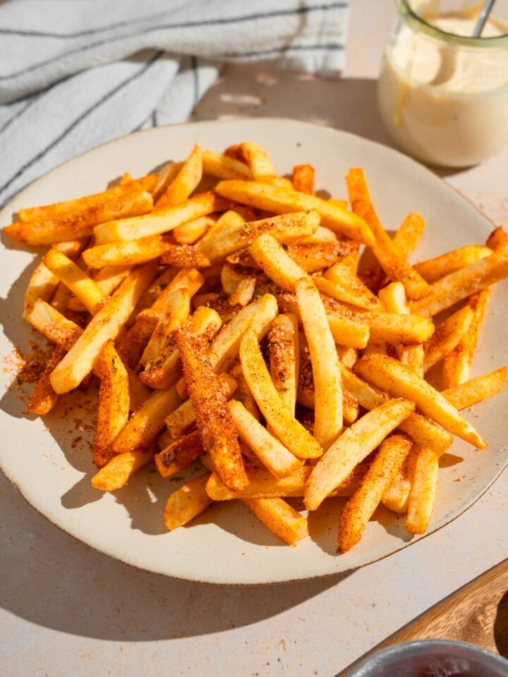 A white plate with Wingstop fries. The plate is on a tan counter with a white striped napkin and small jar of ranch sauce.