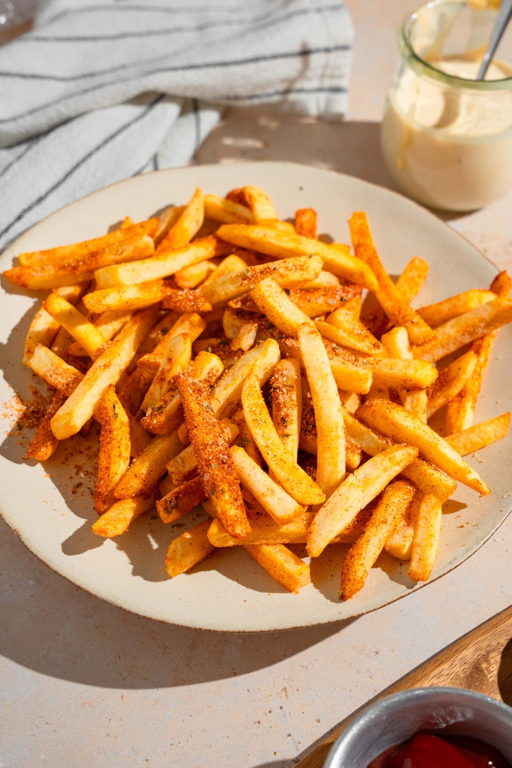 A white plate with Wingstop fries. The plate is on a tan counter with a white striped napkin and small jar of ranch sauce.