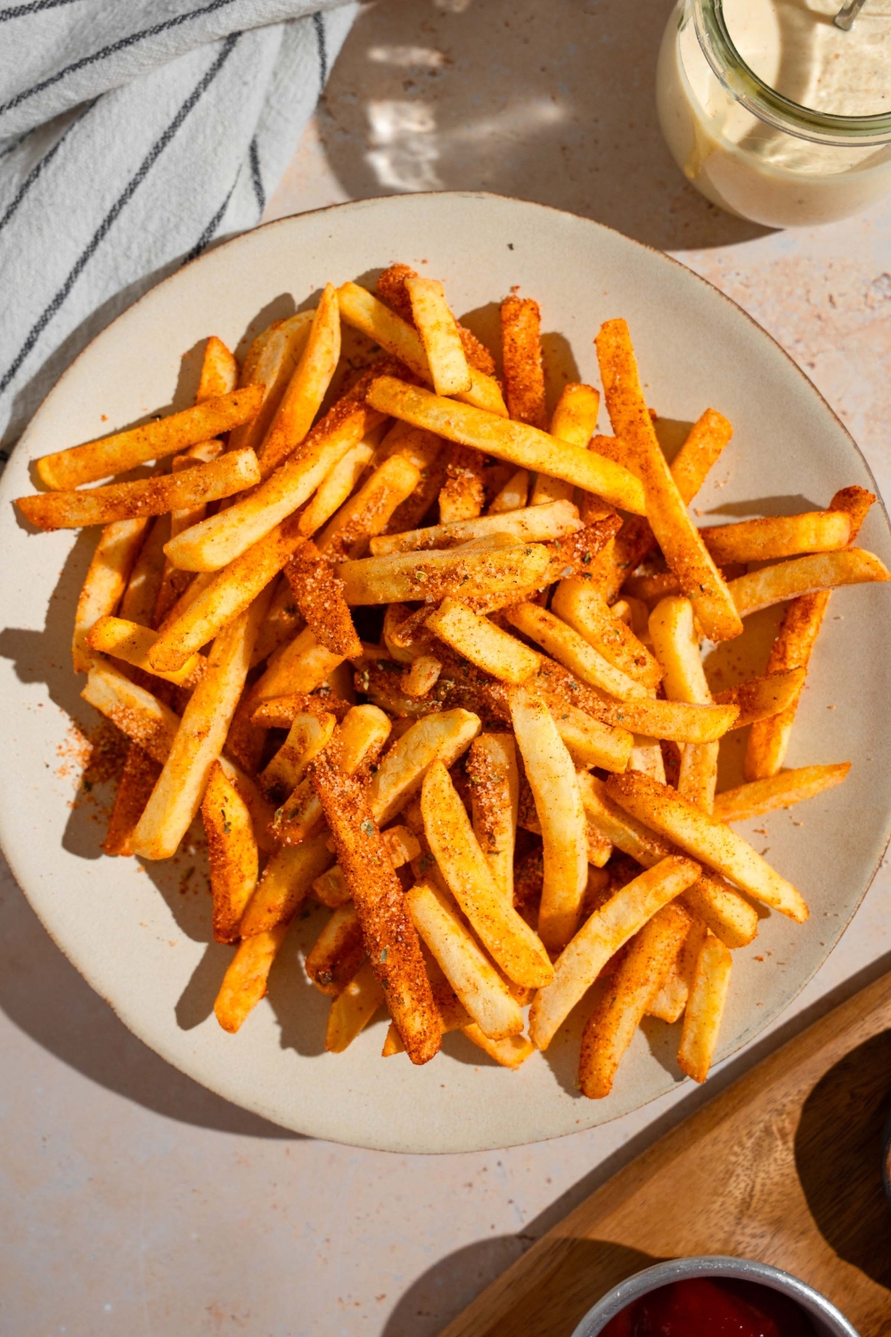 A white plate with Wingstop fries. The plate is on a tan counter with a white striped napkin and small jar of ranch sauce.