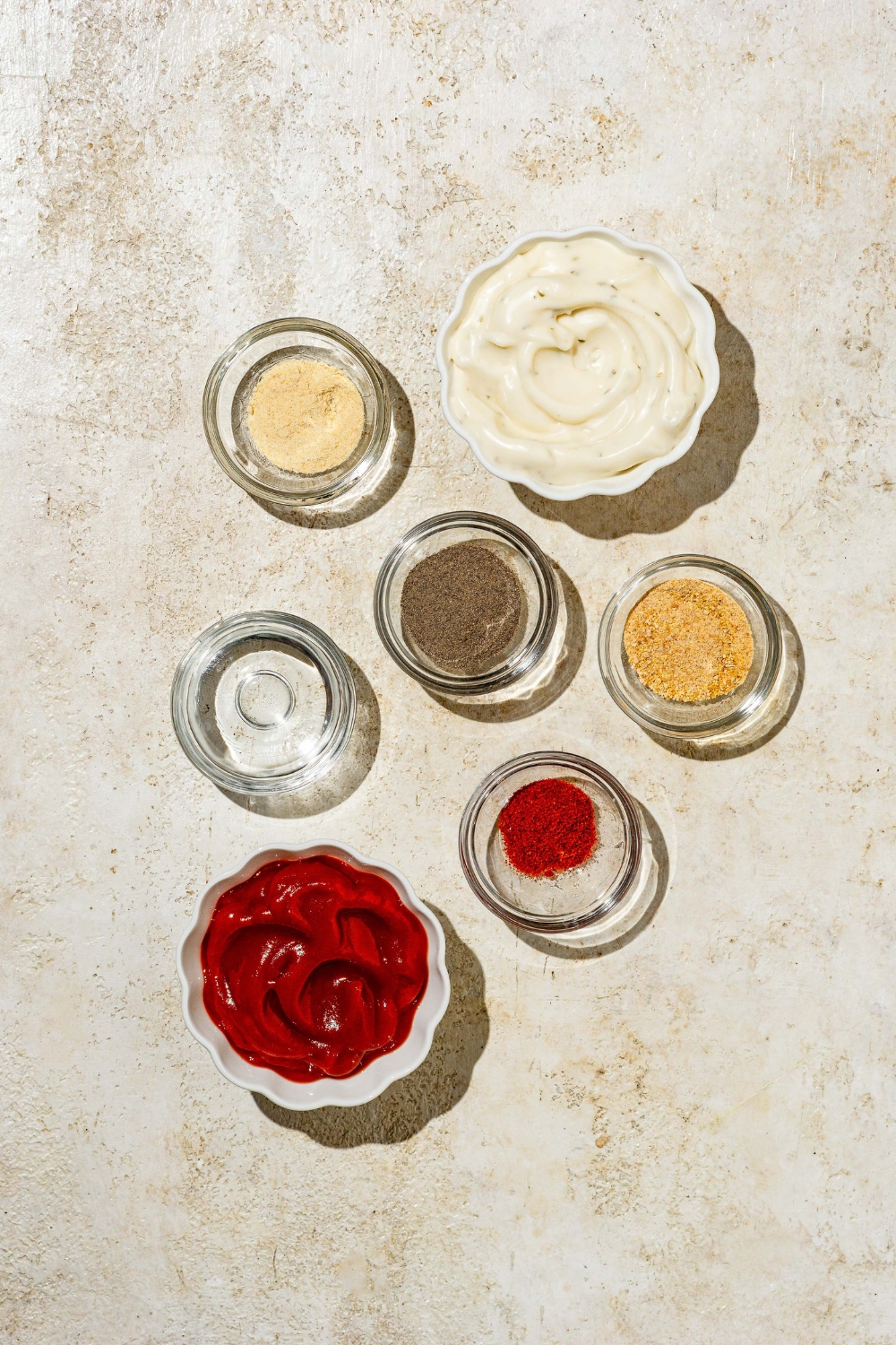 An overhead shot of several bowls containing ingredients to make copycat Zaxby's sauce including ketchup, ranch dressing, vinegar, and seasonings.
