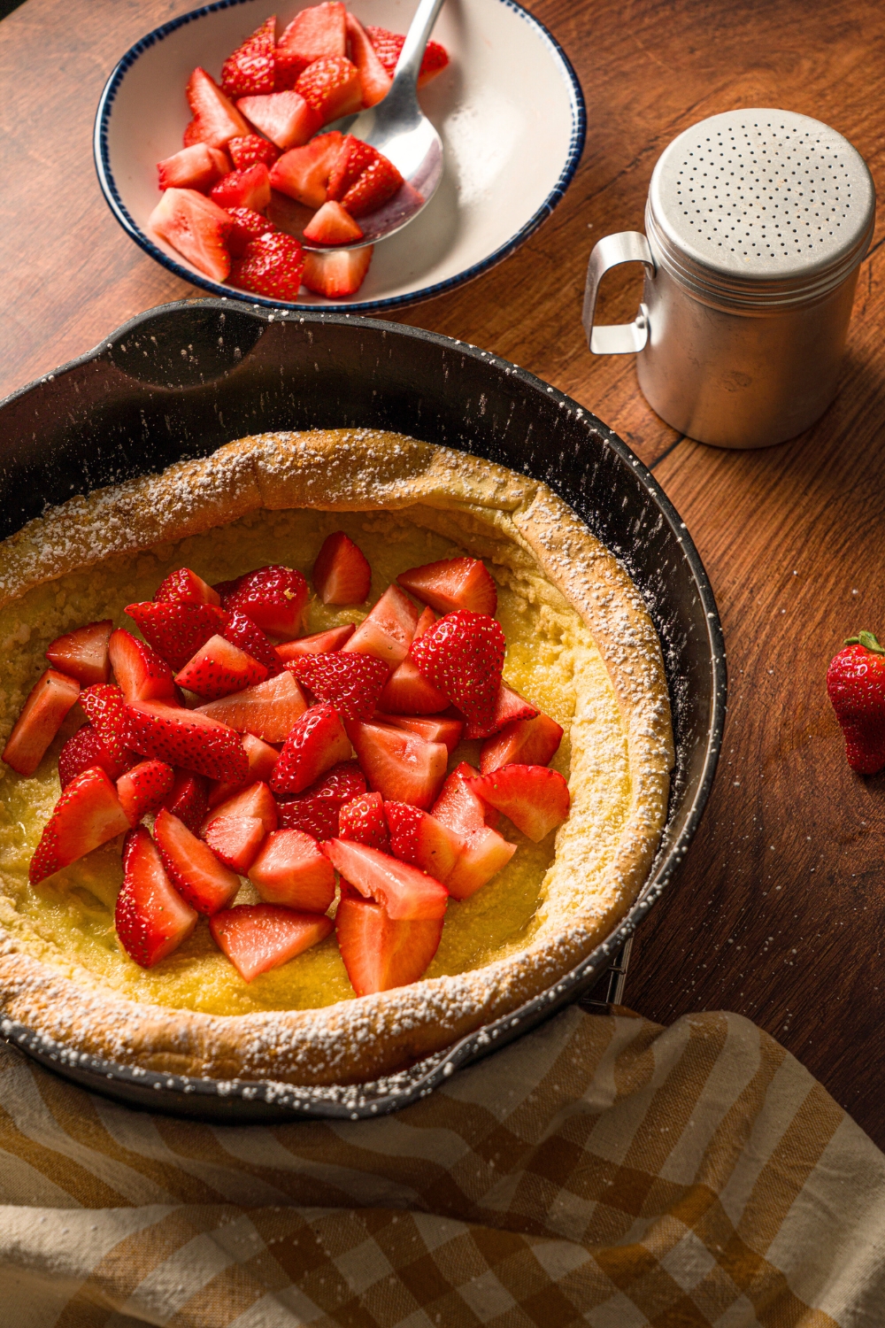 A skillet that has a dutch baby in it with a bunch of sliced strawberries on top