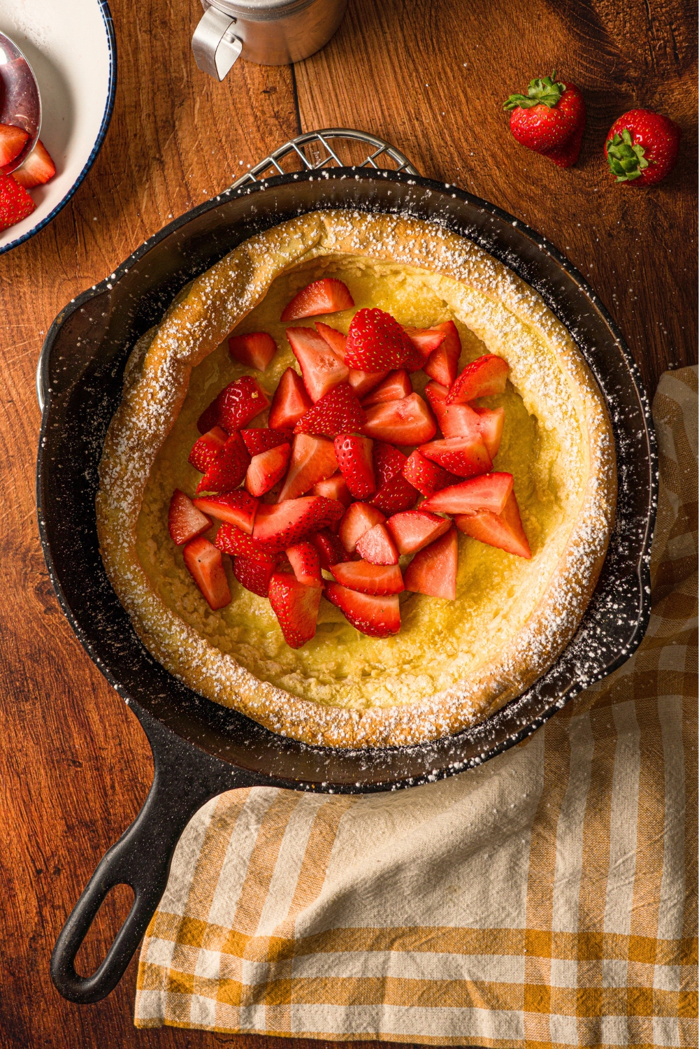 Strawberries on top of a german pancake in a skillet.