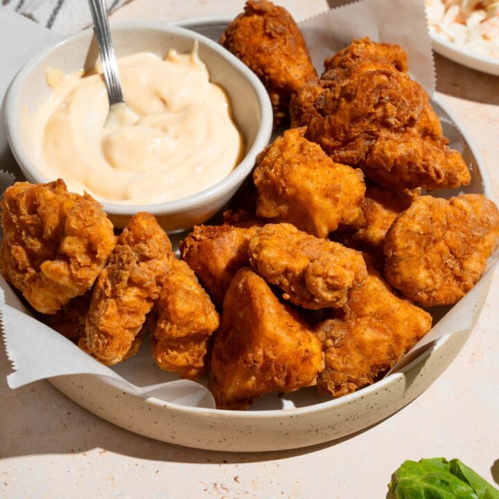 Homemade Chick Fil A nuggets and sauce on a white plate lined with parchment paper. The plate is on a tan counter with a white striped napkin and small plate of coleslaw.