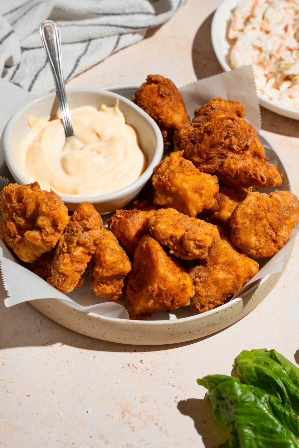 Homemade Chick Fil A nuggets and sauce on a white plate lined with parchment paper. The plate is on a tan counter with a white striped napkin and small plate of coleslaw.