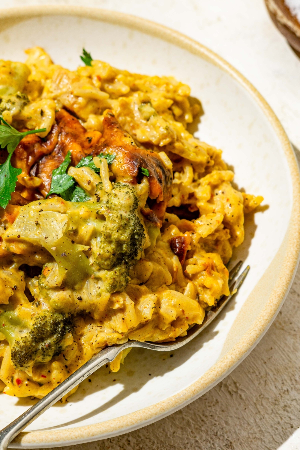 A bowl with chicken broccoli rice casserole garnished with fresh parsley. There is a fork in the bowl. The bowl is on a tan counter.