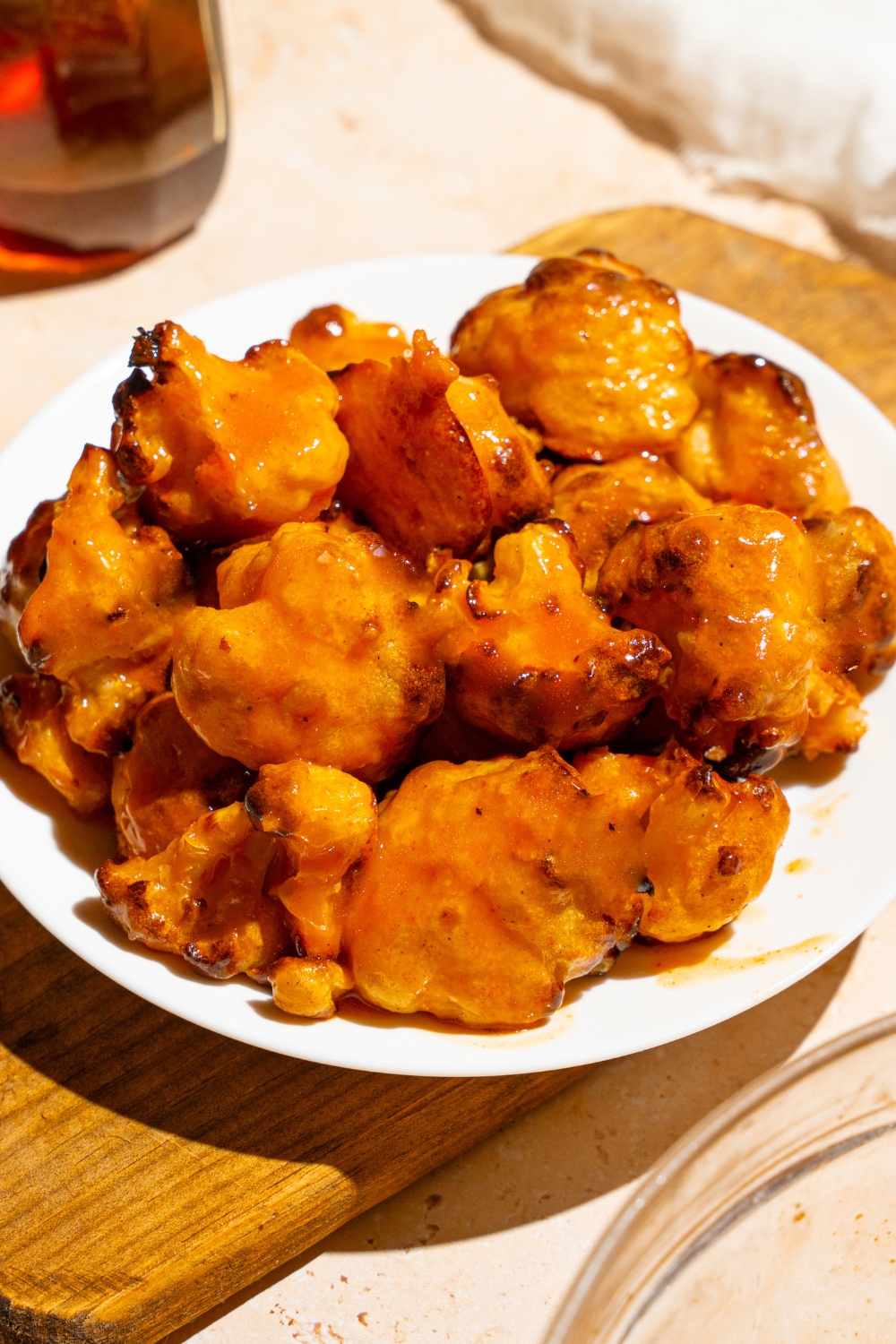 Buffalo cauliflower wings on a white plate on top of a wooden board. The board is on a tan counter.