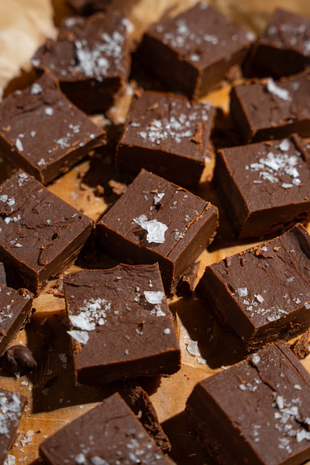 Sliced fudged pieces topped with flaky sea salt on a wooden board lined with parchment paper.