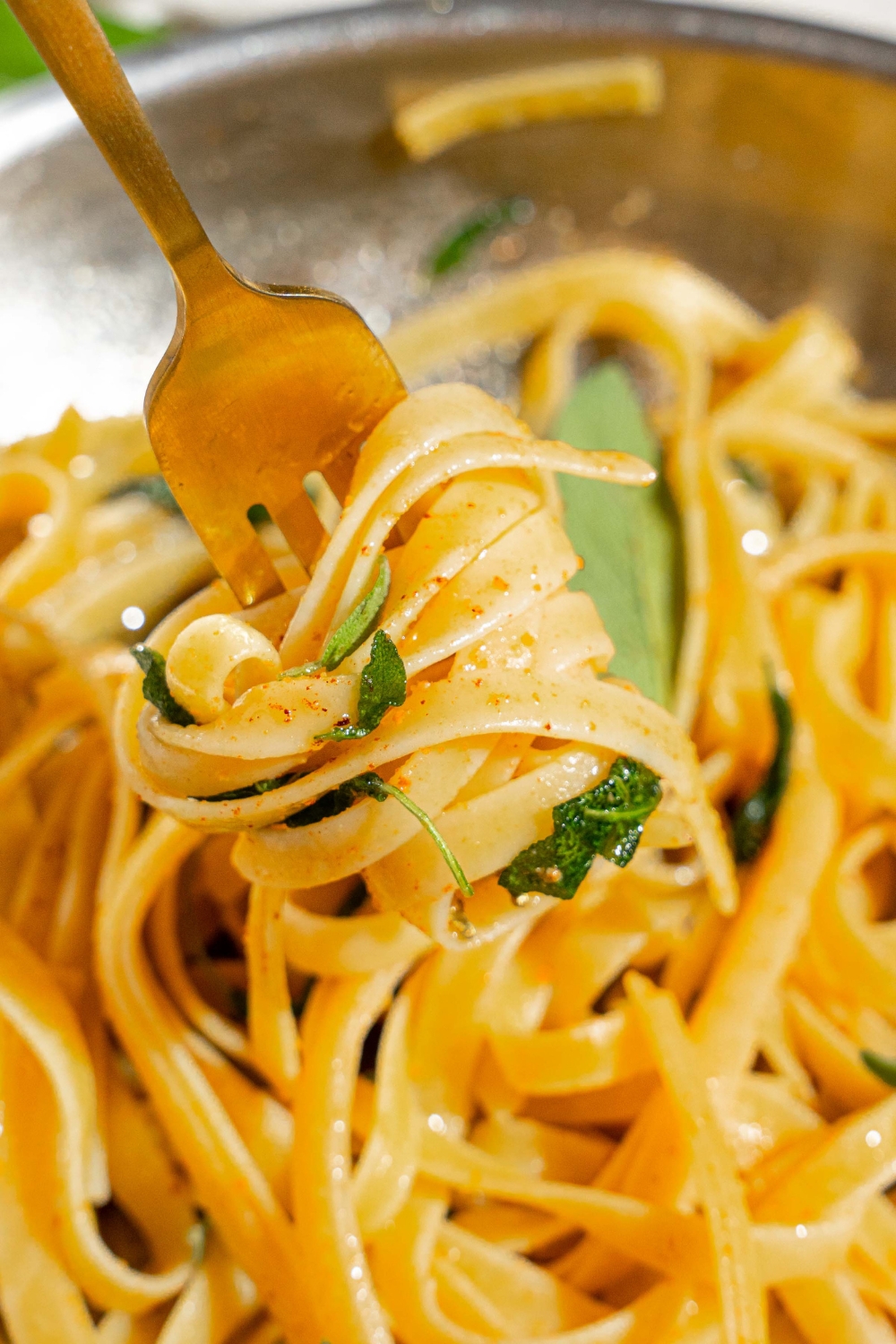 A skillet with a fork twirling a bite of linguine pasta in brown butter sauce with sage.