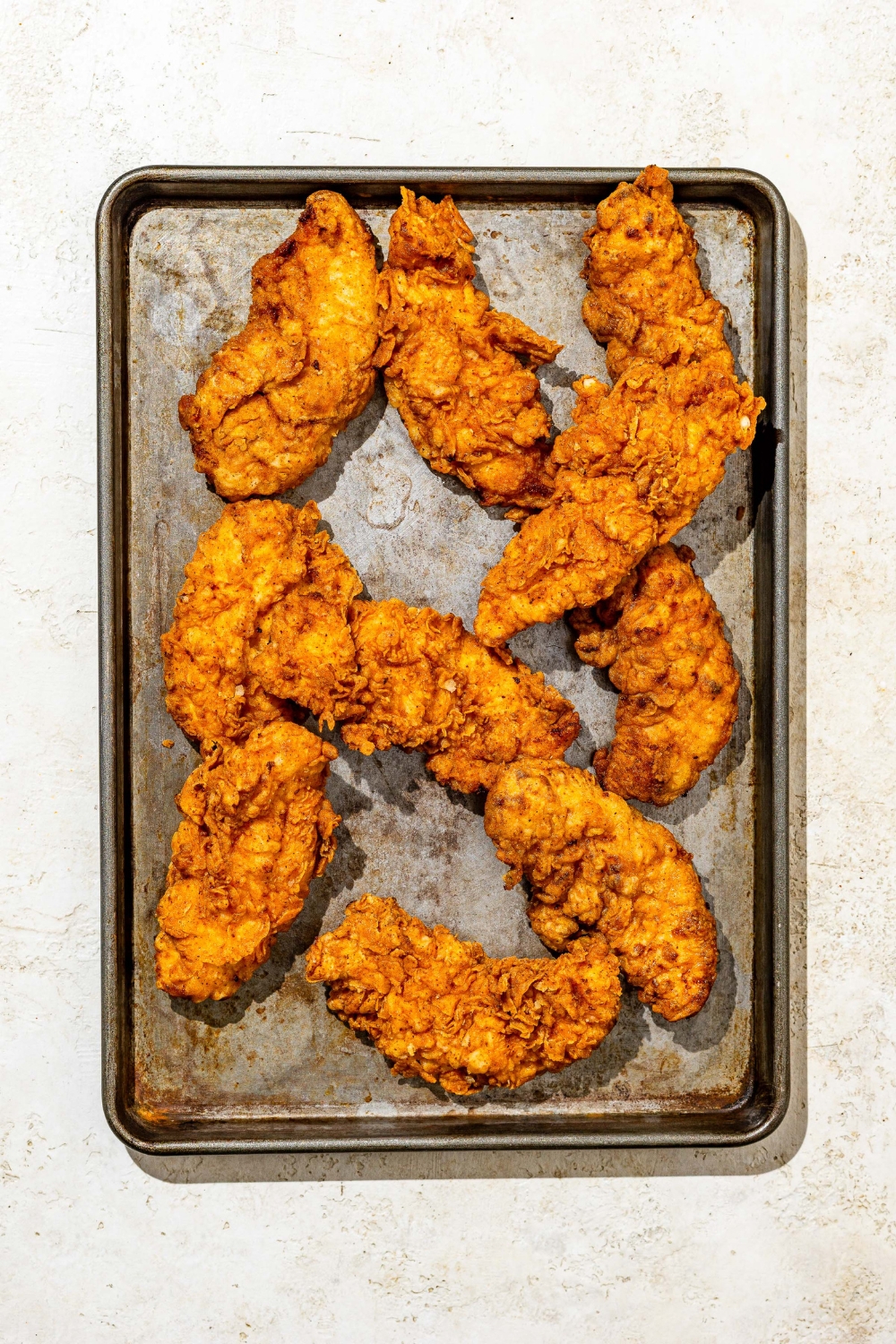 A baking sheet with buttermilk fried chicken tenders. The sheet is on a white counter.