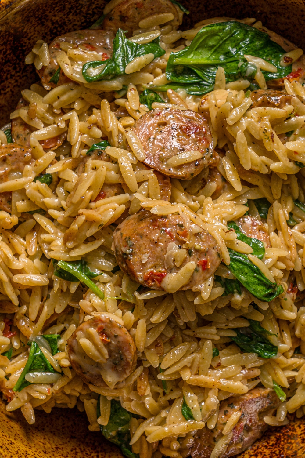 A bowl of chicken sausage orzo pasta tossed with spinach.