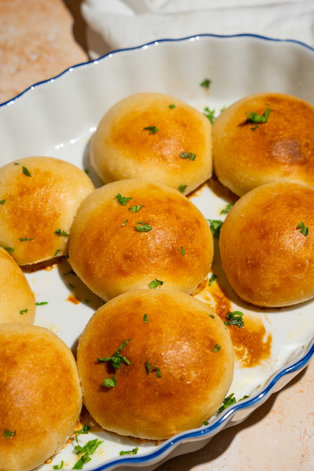 A baking plate with dinner rolls brushed with garlic herb butter and garnished with fresh parsley.