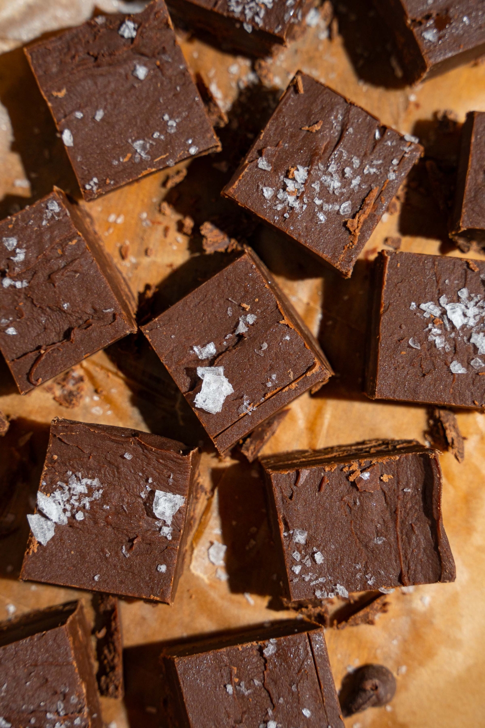 Sliced fudged pieces topped with flaky sea salt on a wooden board lined with parchment paper.