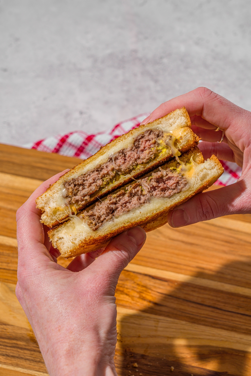 A hand holding a sliced copycat Applebee's grilled cheeseburger with a wooden board on a stone counter in the background.