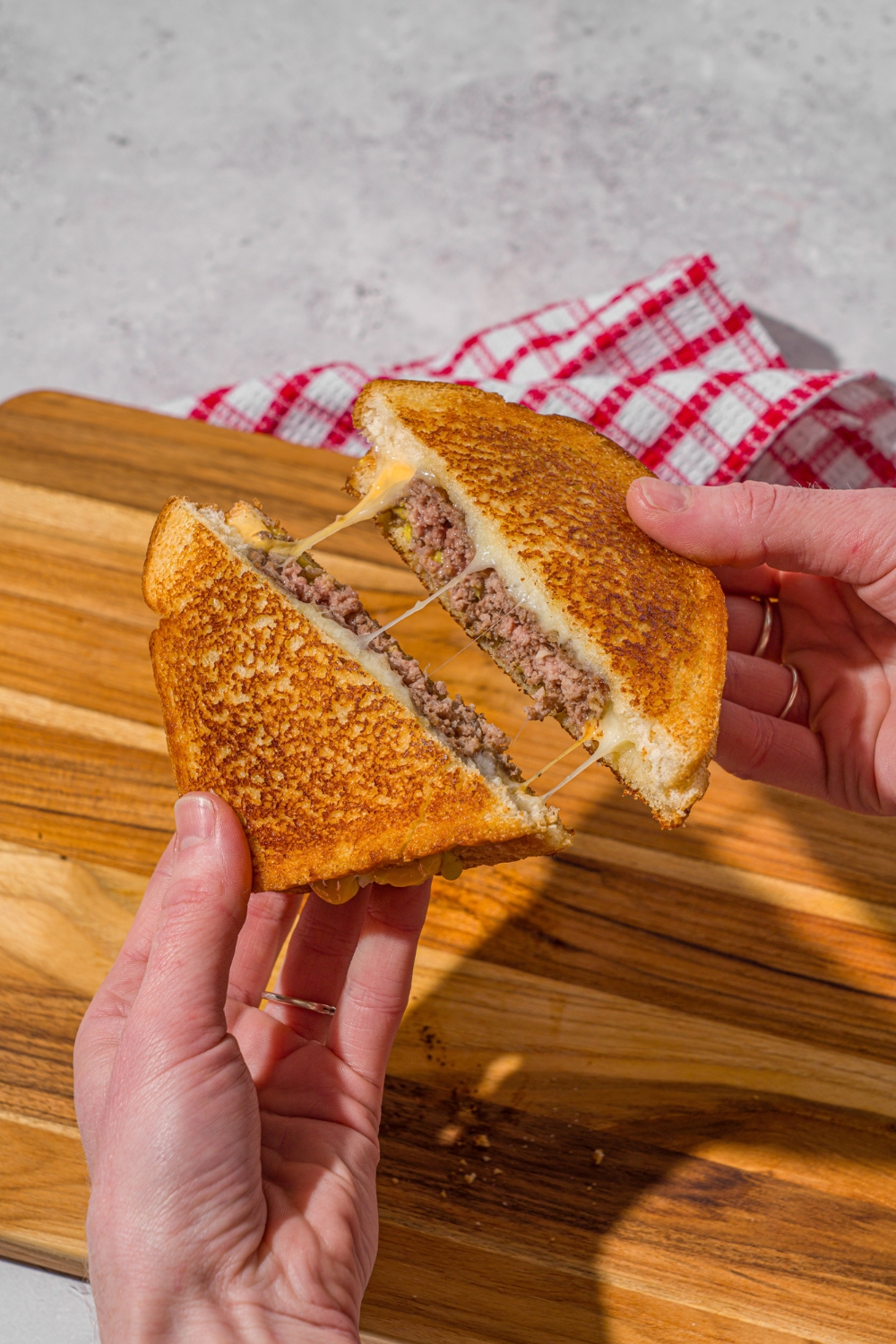 A hand pulling apart a copycat Applebee's grilled cheeseburger. There is a wooden board on a stone counter in the background.