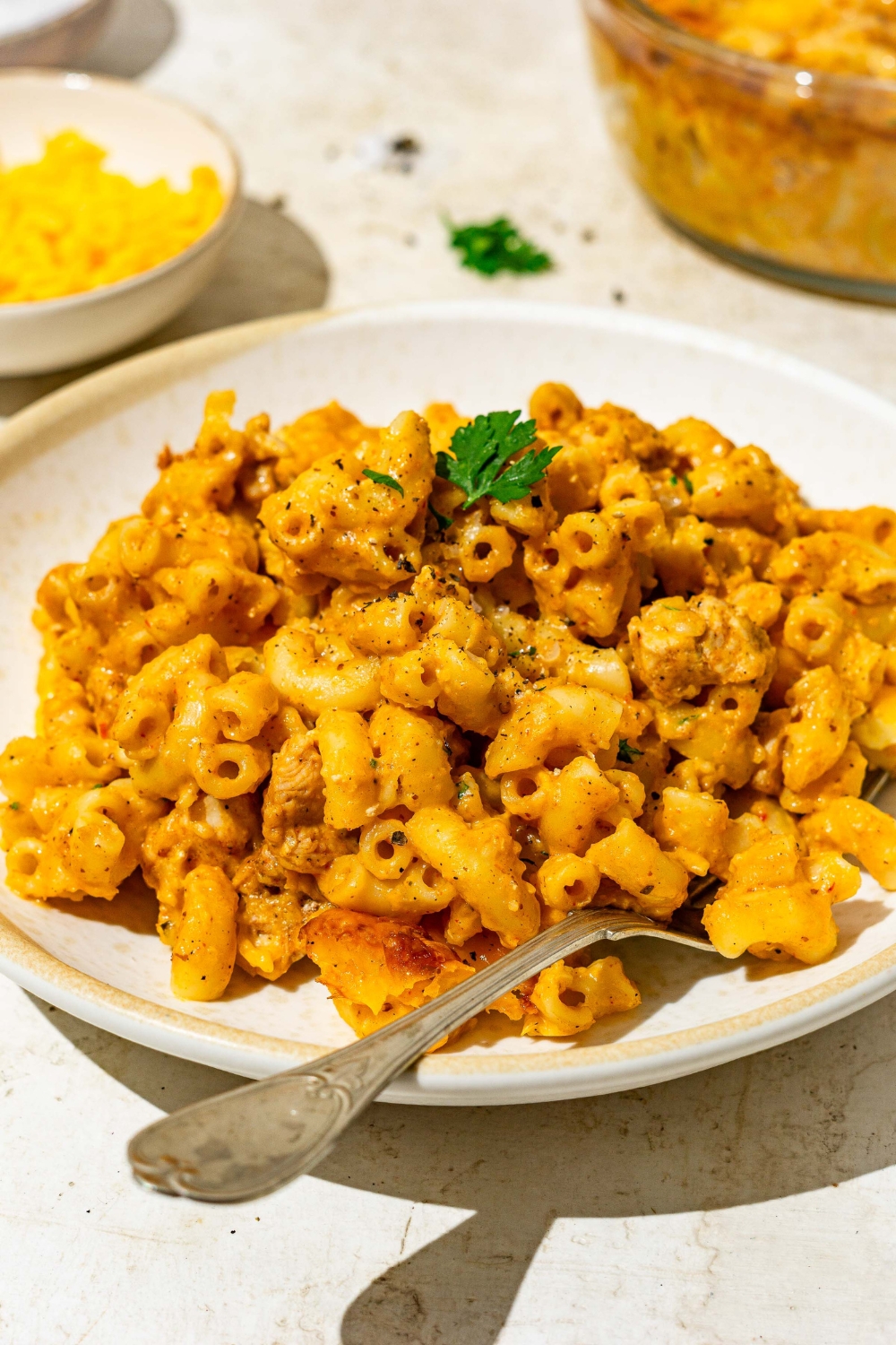 A plate of Buffalo mac and cheese garnished with fresh parsley. The plate is served with a fork. The plate is on a tan counter.