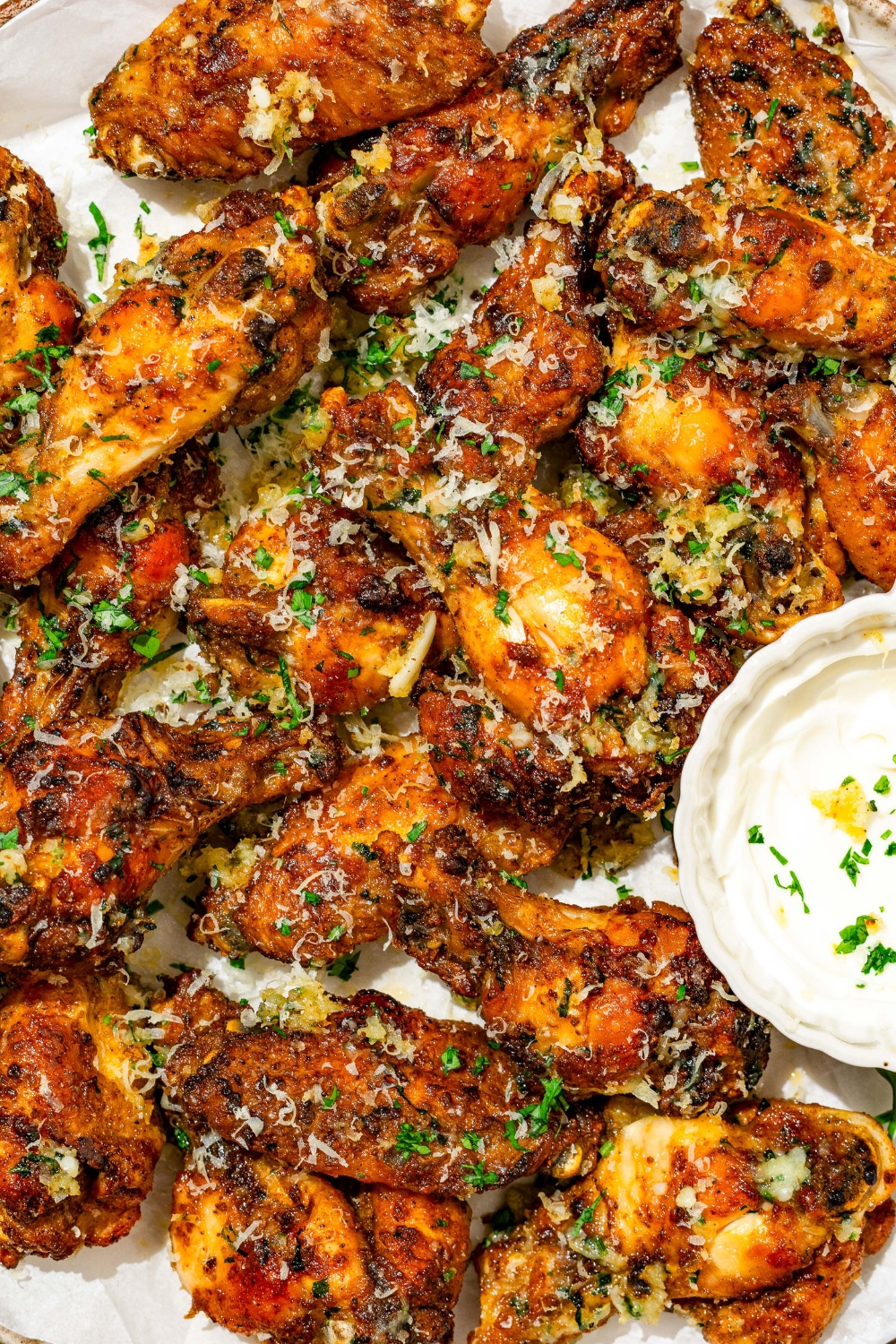 A plate of copycat Wingstop garlic parmesan chicken wings garnished with grated cheese and fresh parsley. There is a bowl of sauce on the plate.