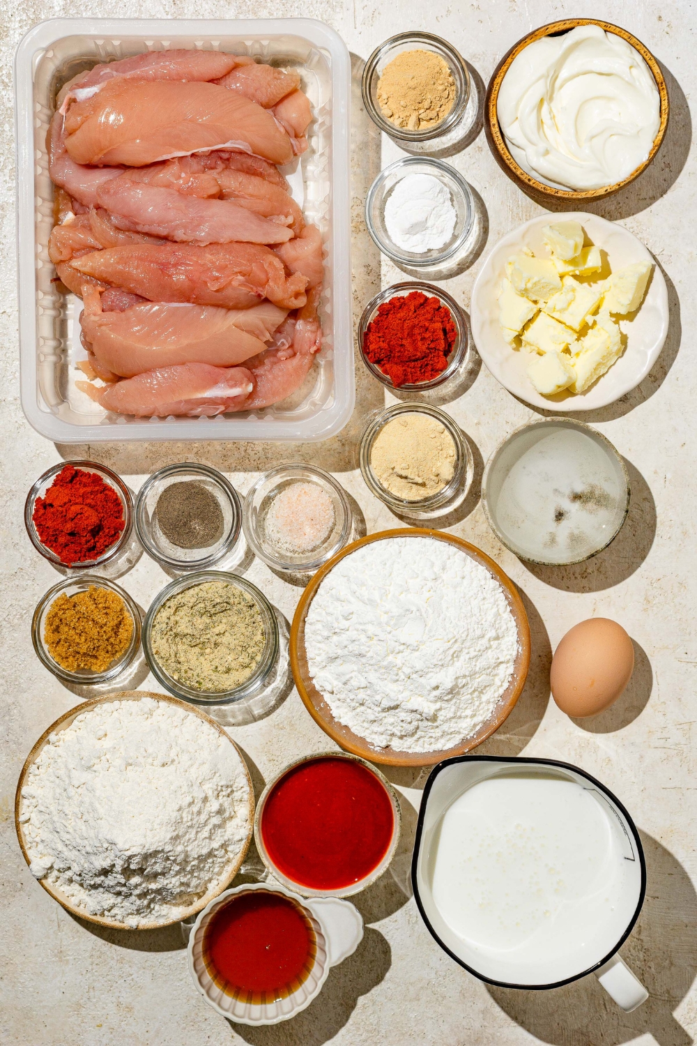 An overhead shot of several bowls in various sizes containing ingredients to make copycat Wingstop hot honey chicken tenders including chicken tenders, honey, flour, butter, cornstarch, hot sauce, buttermilk, mayo, and seasonings.