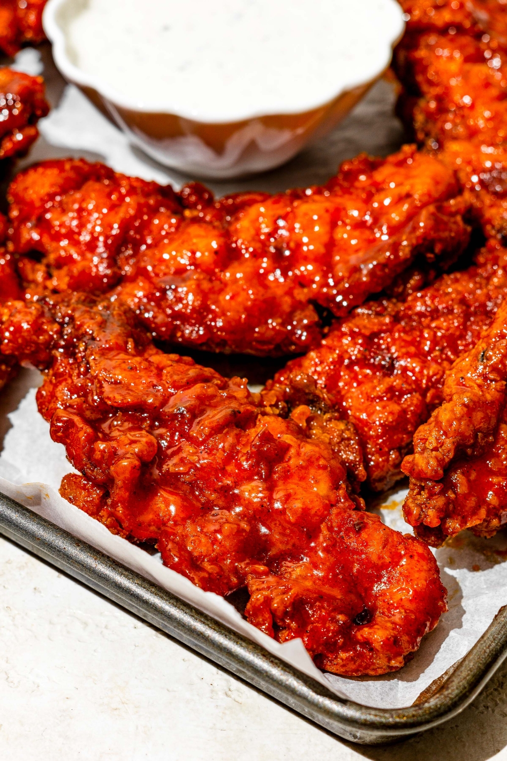 A baking sheet lined with parchment paper with copycat Wingstop hot honey chicken tenders with a small bowl of ranch sauce.