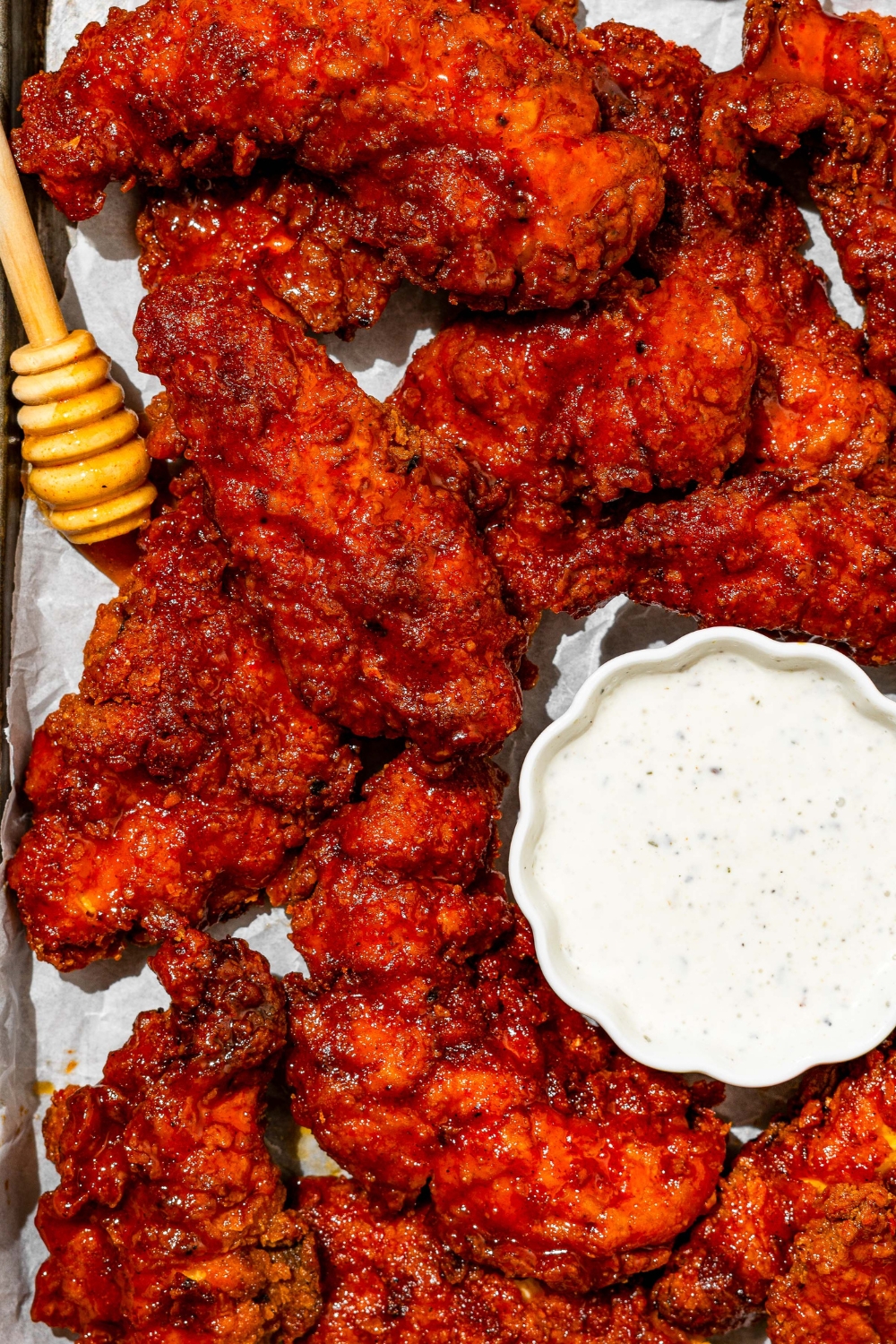 A baking sheet lined with parchment paper with copycat Wingstop hot honey chicken tenders with a small bowl of ranch sauce.