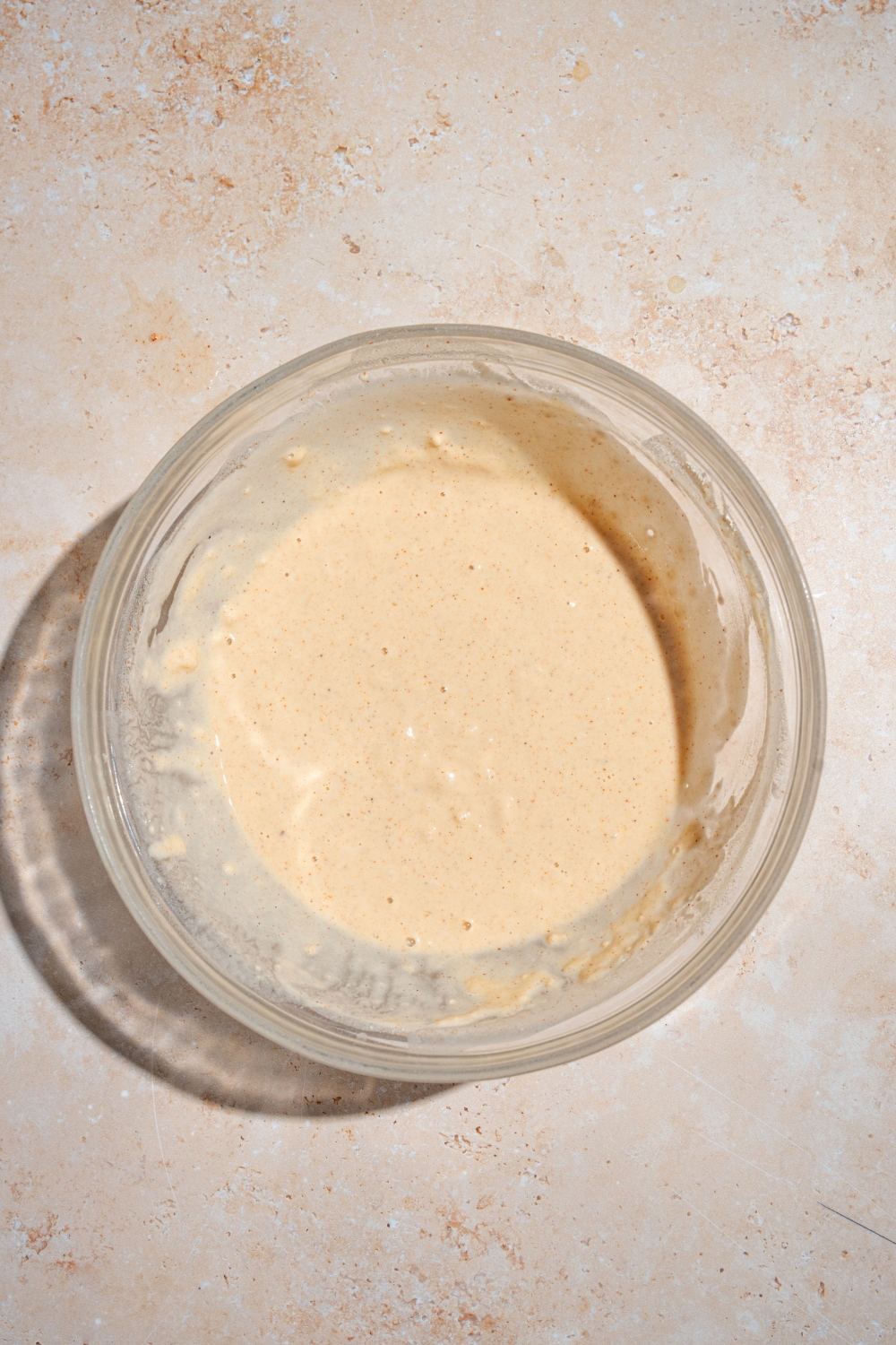 A glass bowl of seasoned batter mixture. The bowl is on a tan counter.