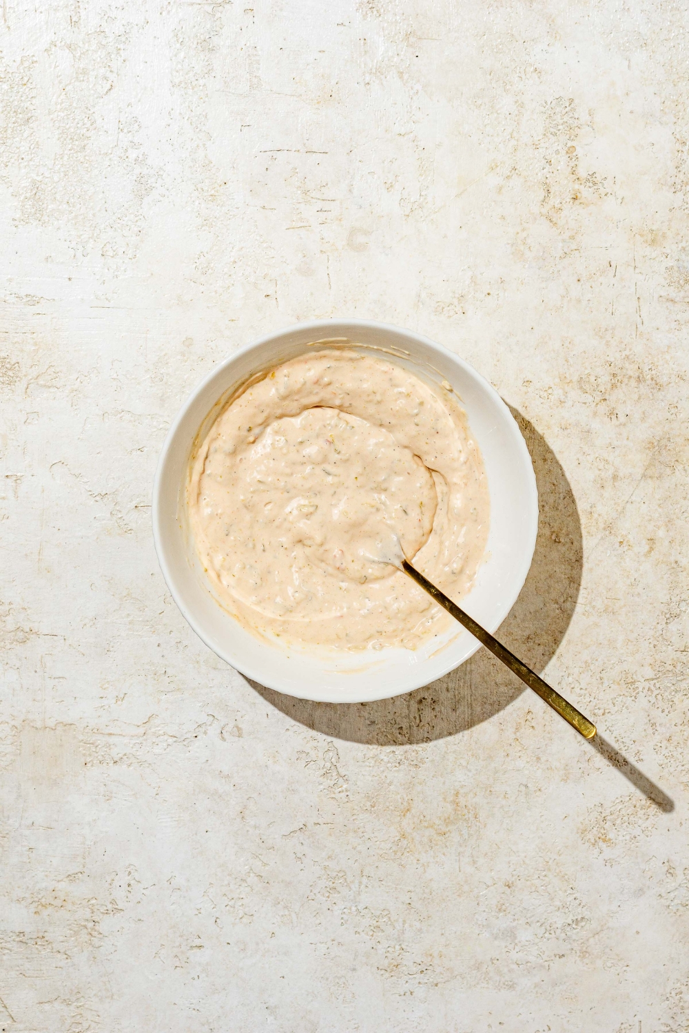 A small bowl of a spoon mixing In n Out animal style sauce. The bowl is on a tan counter.