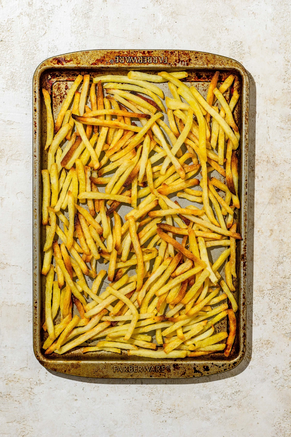 A baking sheet of baked fries. The sheet is on a tan counter.