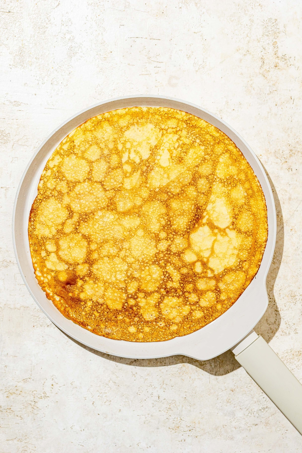 A skillet with a flipped cooked Swedish pancake. The skillet is on a white counter.