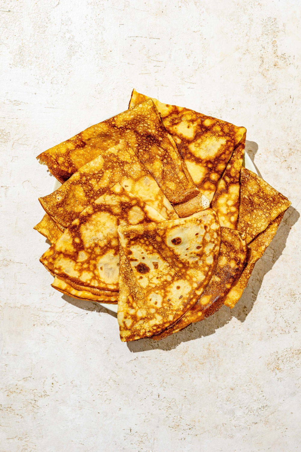 A white plate with several Swedish pancakes stacked on one another. The plate is on a white counter.