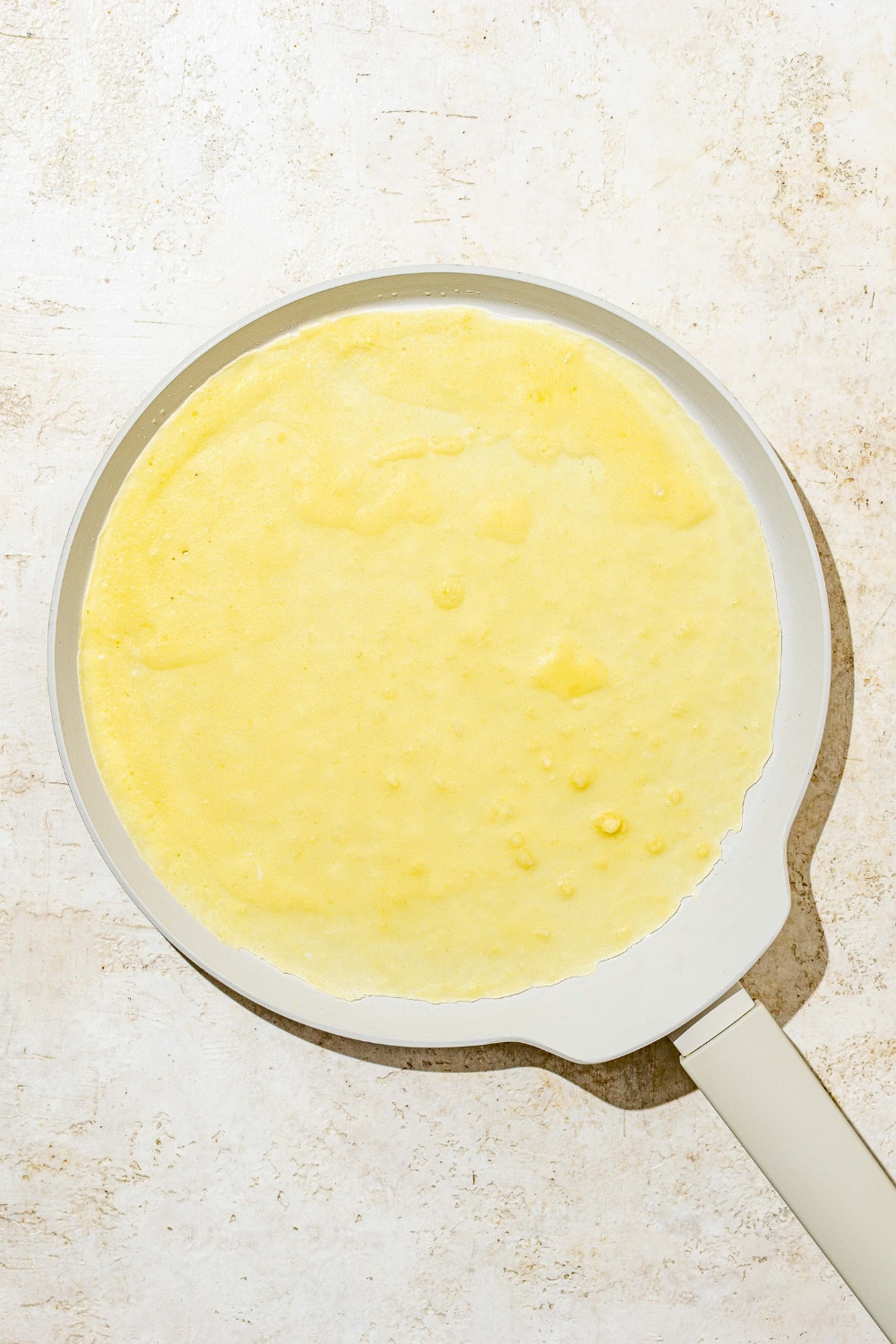 A skillet with one side of a Swedish pancake cooking in butter. The skillet is on a white counter.