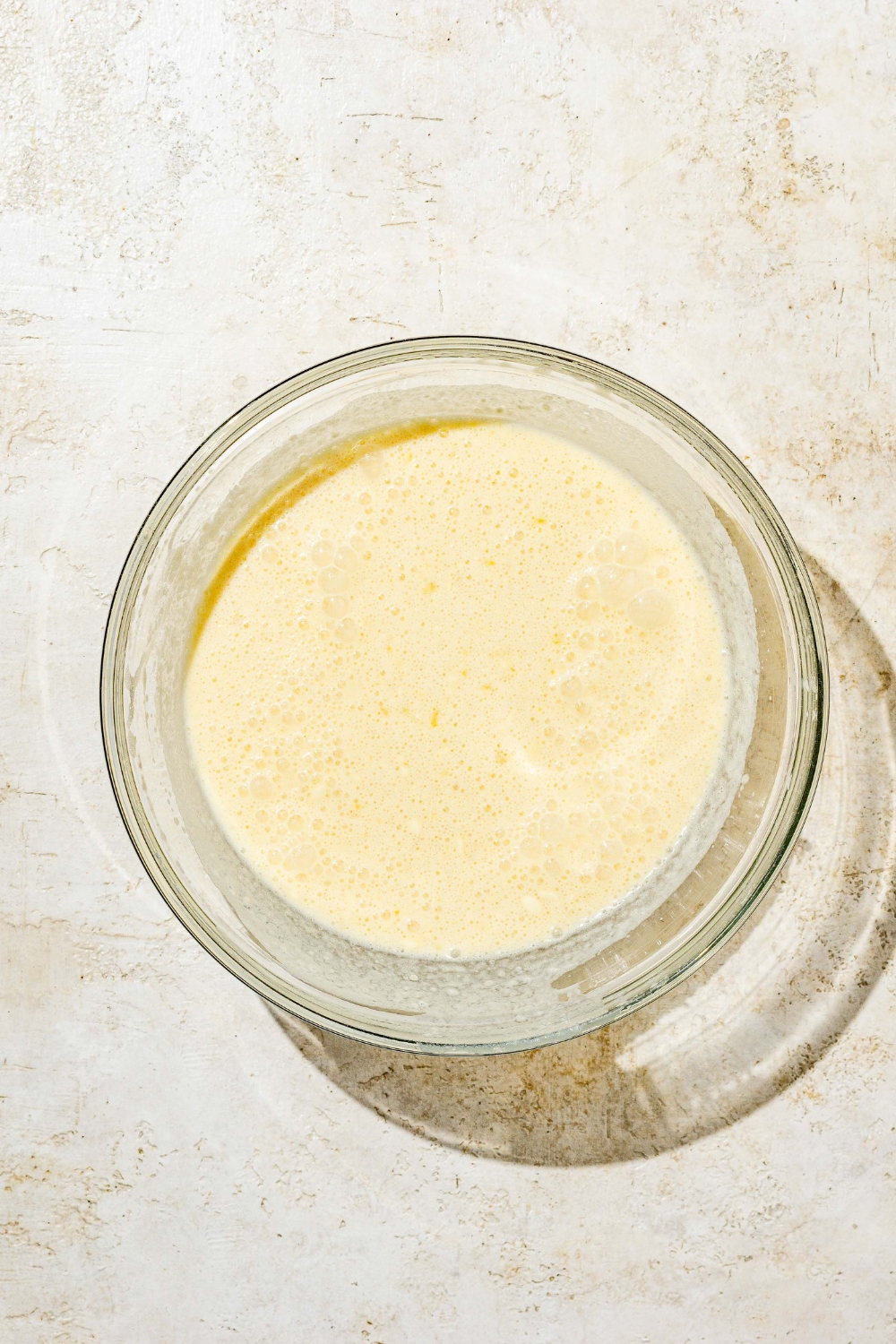 A glass bowl with blended Swedish pancake batter. The bowl is on a white counter.