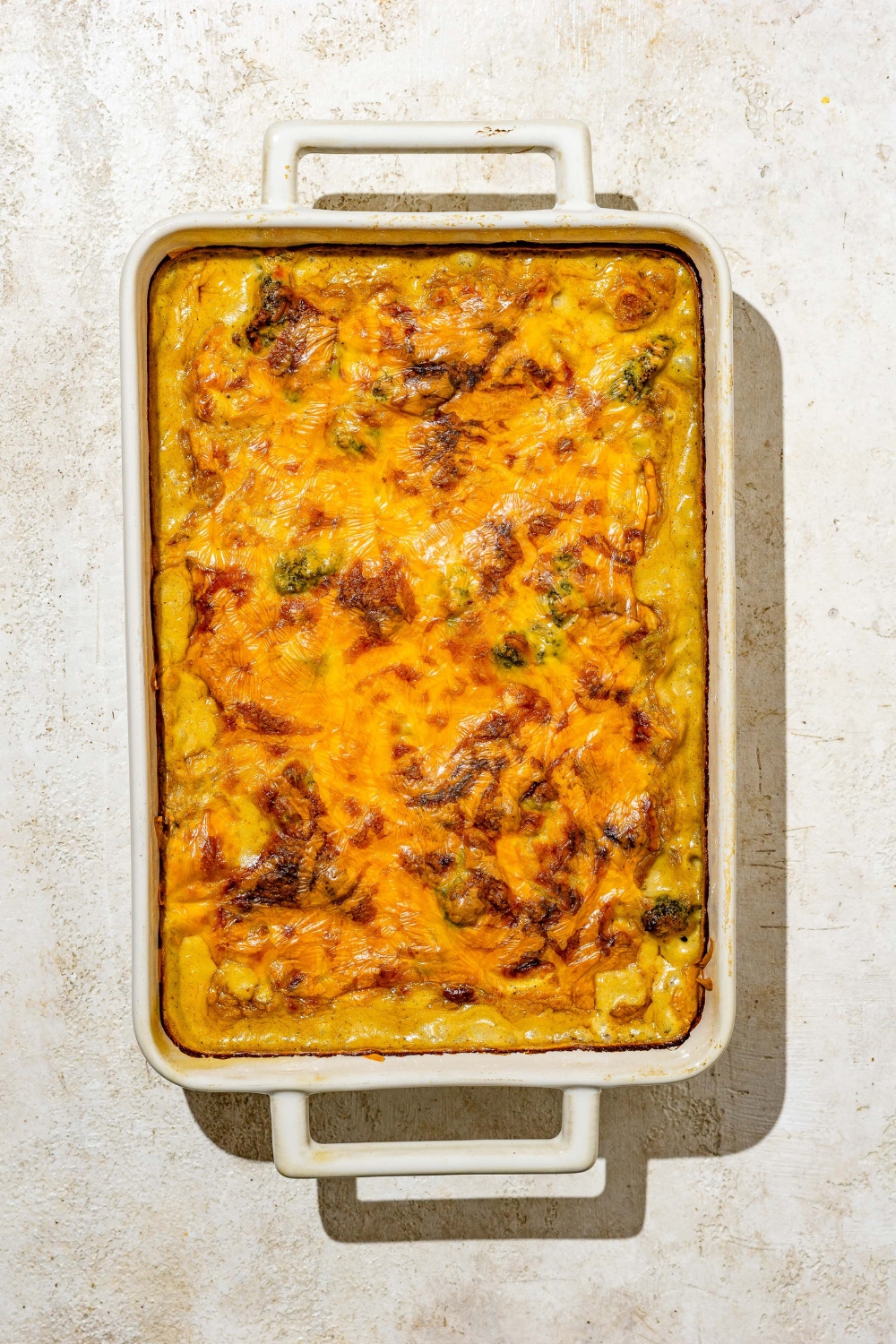 A baking dish with baked chicken broccoli rice casserole. The dish is on a tan counter.