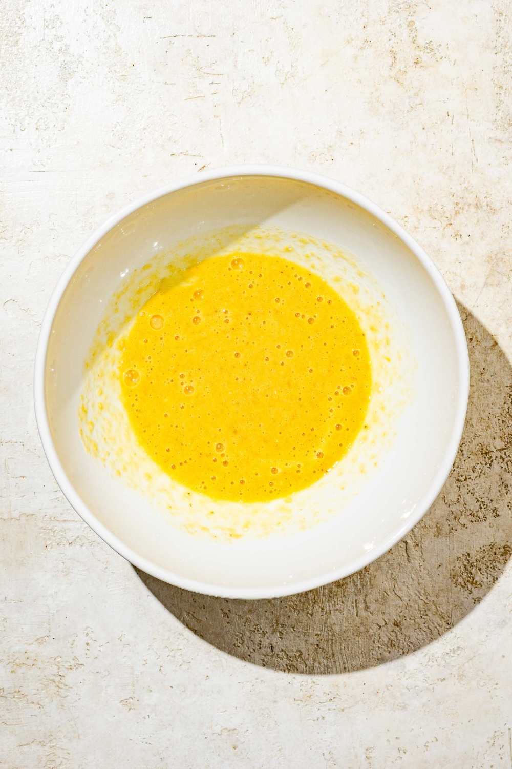 A white bowl with wet ingredient mixture for banana smash cake. The bowl is on a tan counter.