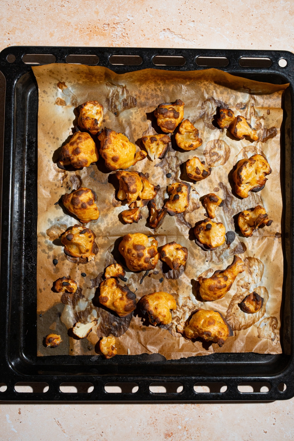 A baking sheet lined with parchment paper with baked battered cauliflower florets. The baking sheet is on a tan counter.