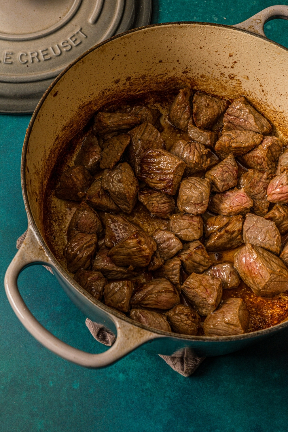 A dutch oven with browned cubed beef. The dutch oven is on a blue counter.