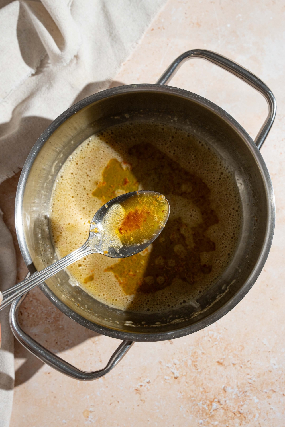 A sauce pan with browned butter and a spoon with some butter. The pot is on a tan counter.