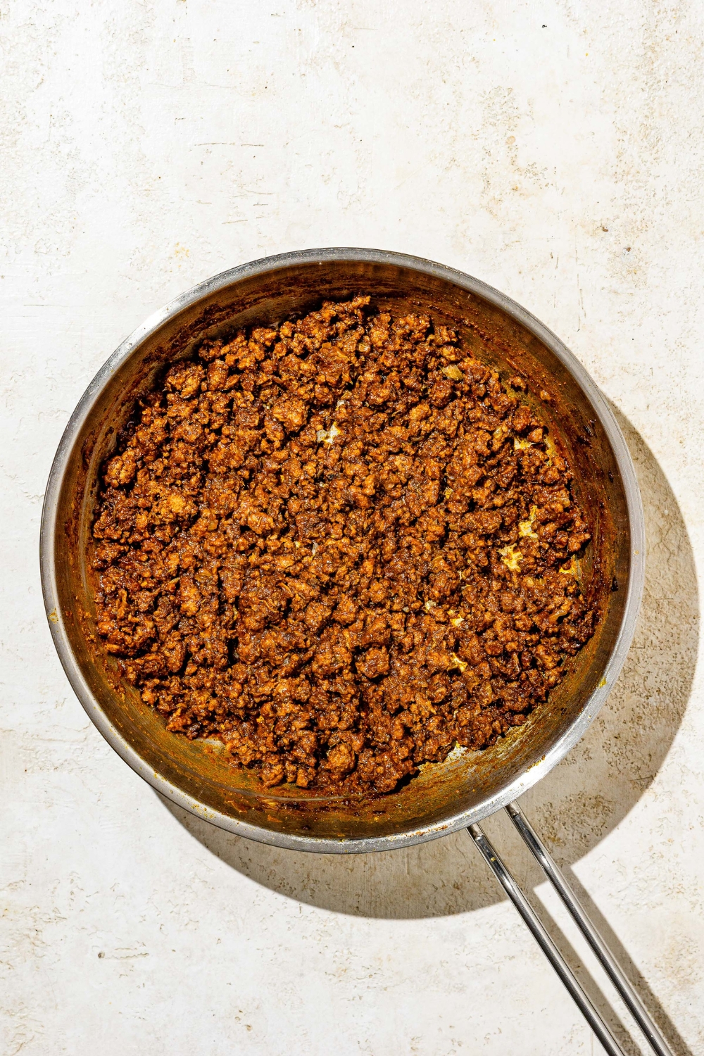 A skillet with cooked ground beef tossed in seasonings. The skillet is on a tan counter.