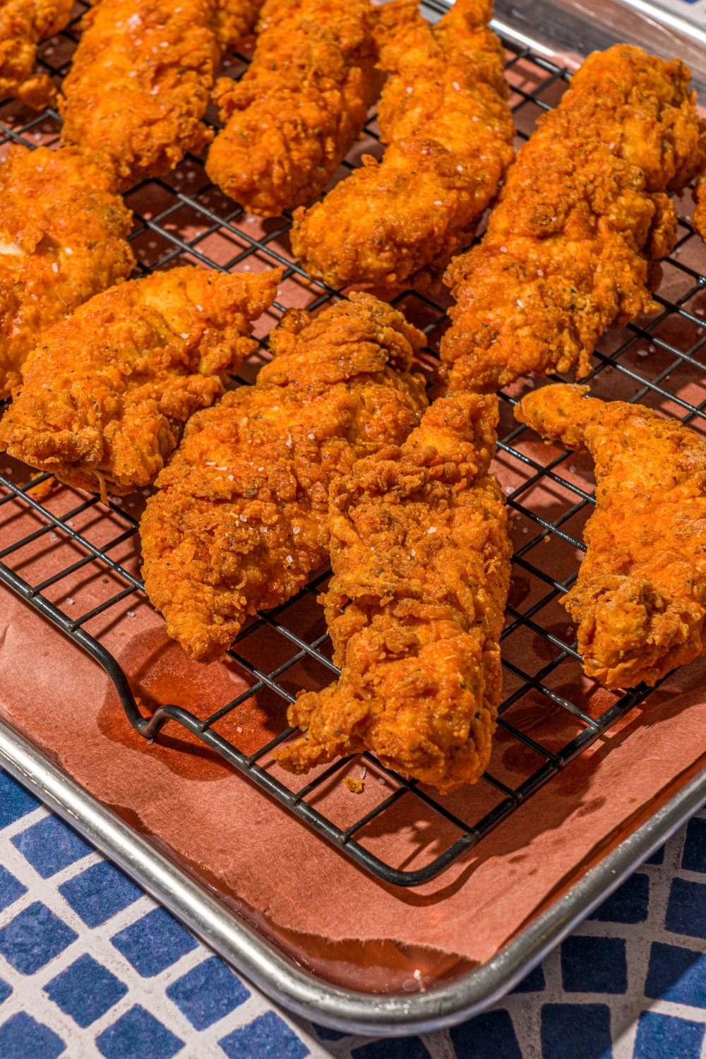 A baking sheet lined with parchment paper with a rack of crispy chicken tenders.