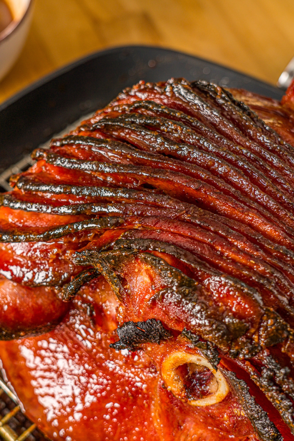 A close up of a glazed spiral ham in a roasting pan lined with a rack.