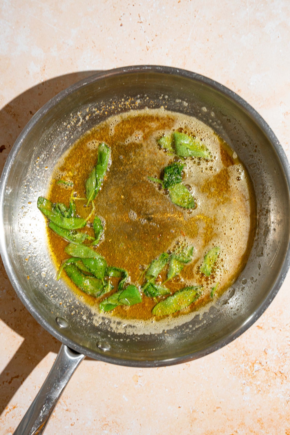 A skillet with sage cooking in browned butter. The skillet is on a tan counter.