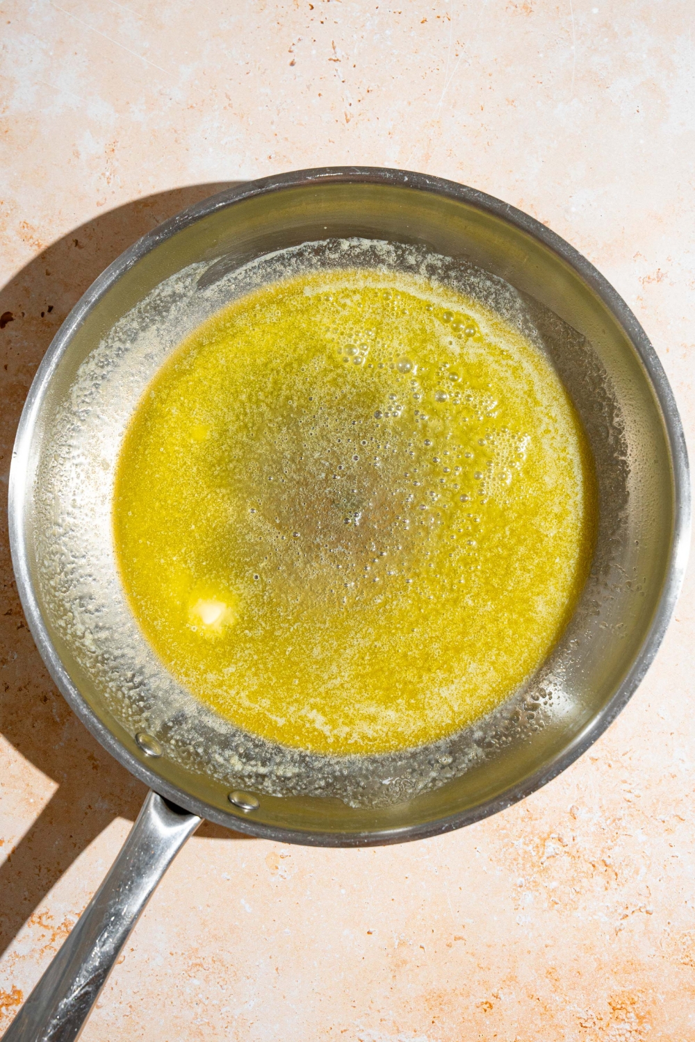 A skillet with melted butter. The skillet is on a tan counter.