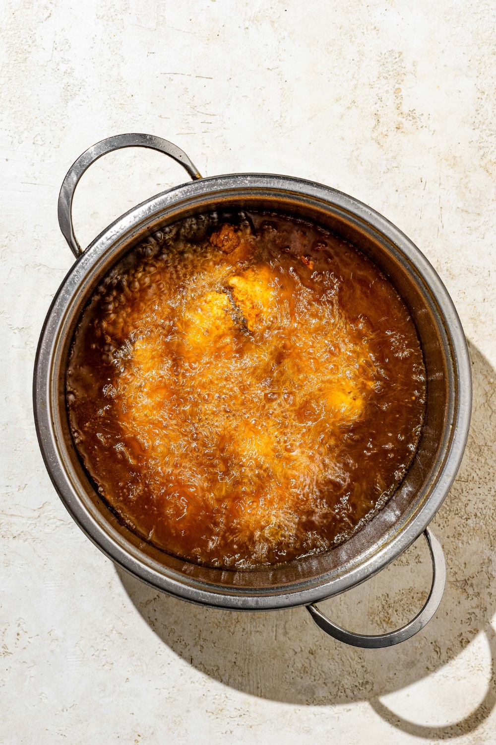 A stock pot of breaded chicken tenders frying in oil. The pot is on a white counter.