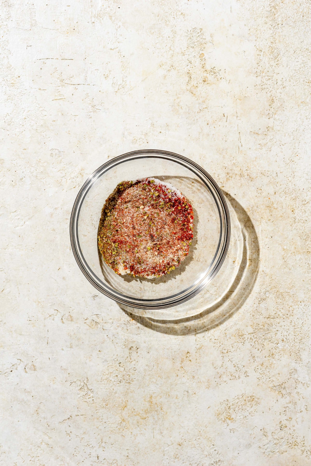 A small bowl with ingredients combined to make cajun seasoning including smoked paprika, garlic powder, onion powder, thyme, salt, and pepper. The bowl is on a white counter.